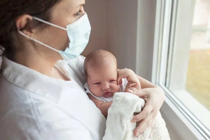 A Mama wearing a mask while feeding her baby
