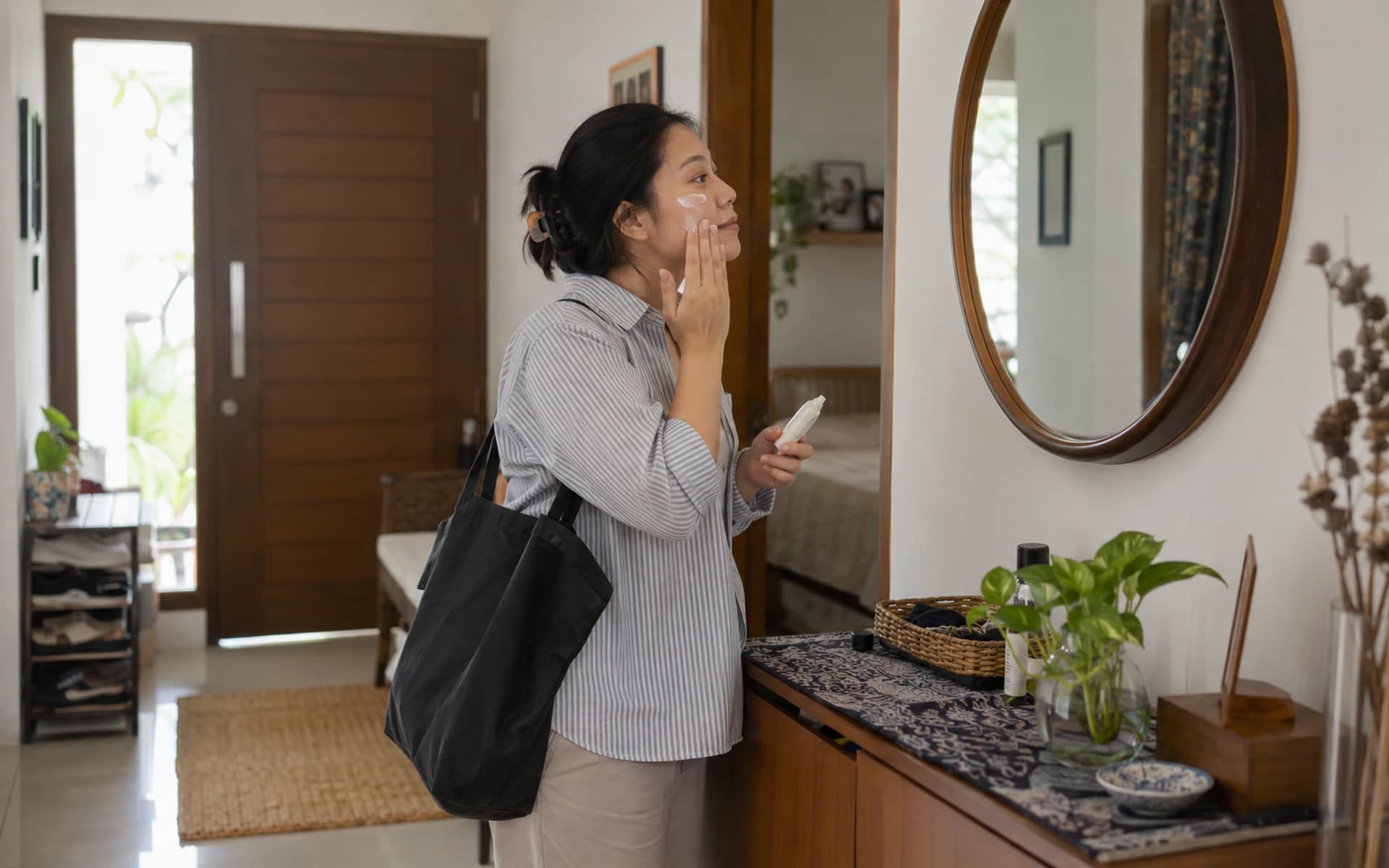 Perempuan mengoleskan perawatan wajah di depan cermin sebelum keluar rumah