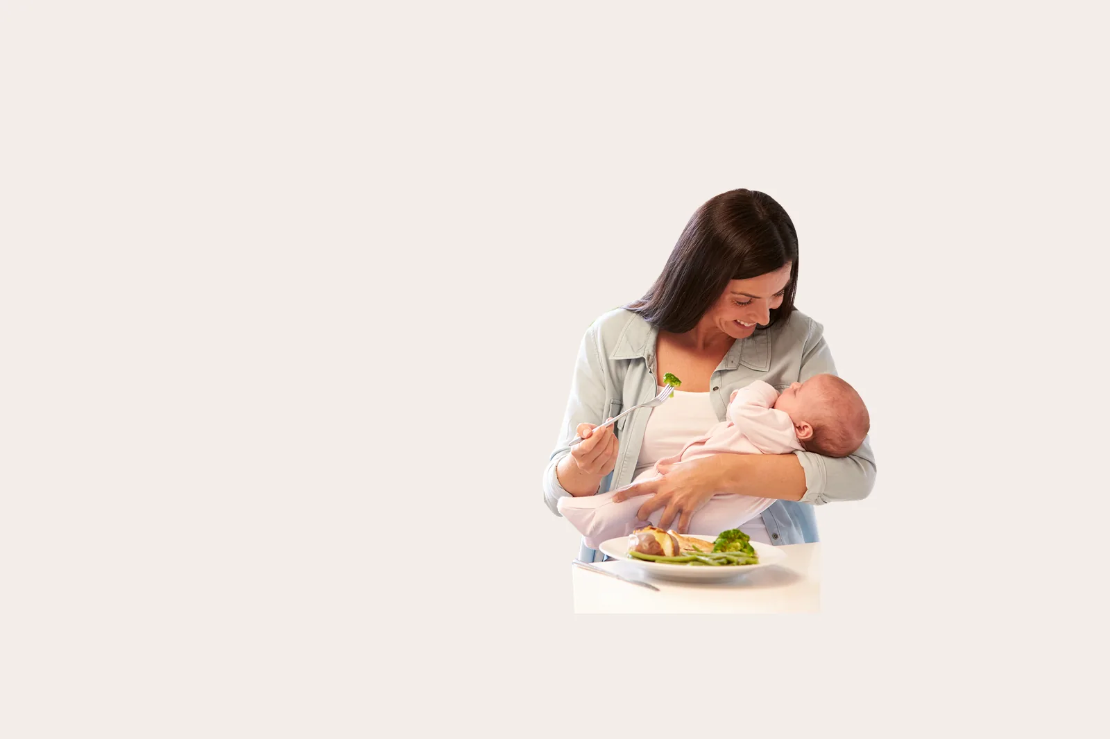 Ibu menyusui menyantap makanan sehat sambil menggendong bayinya
