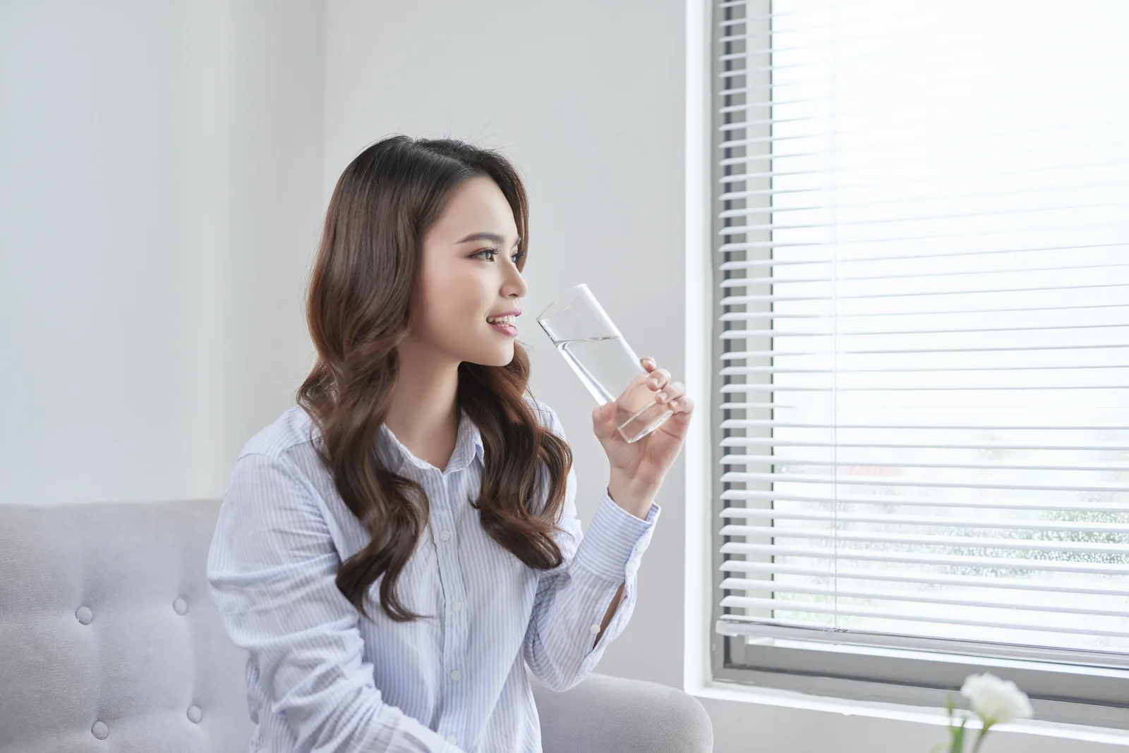 Perempuan minum air di dekat jendela