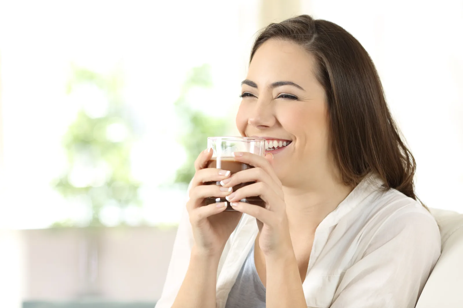 Perempuan tertawa sambil memegang gelas